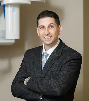 Dr. Tal Lebel, smiling, arms crossed, in a dark blazer